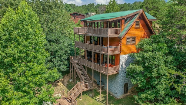 A multi-story log cabin with a balcony and a staircase, surrounded by dense forest. - FlatBackyard, FirePit, HotTub, Horseshoes, games, 60-game arcade FUN 4 FAMILIES! (Sevierville)