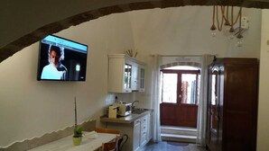 A kitchen with a TV mounted on the wall, a dining table with chairs, and a wooden cabinet. - Tourist Location Joy's Home (Bari)