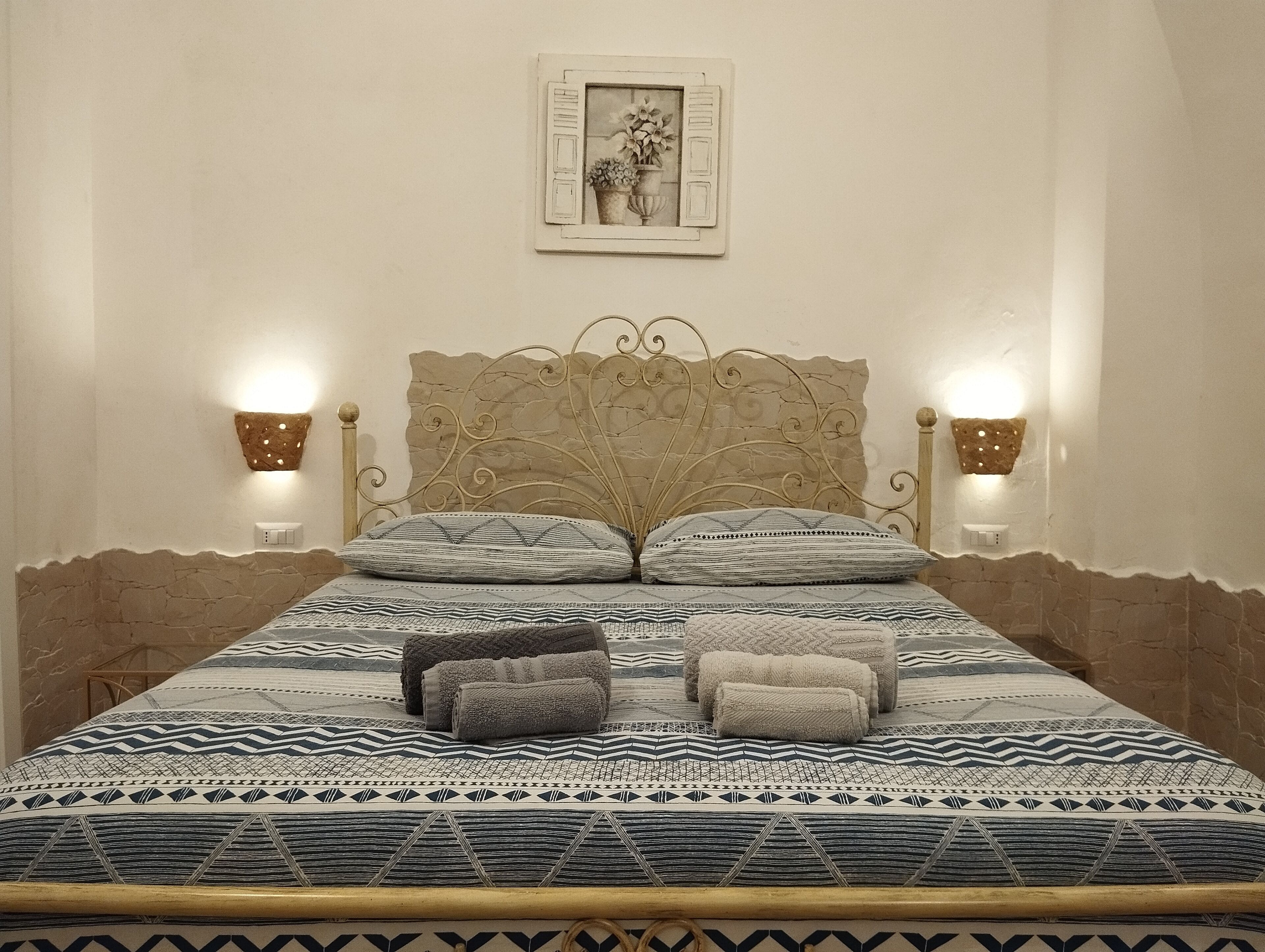 Un letto con una coperta a motivi, due cuscini e due lampade a parete.