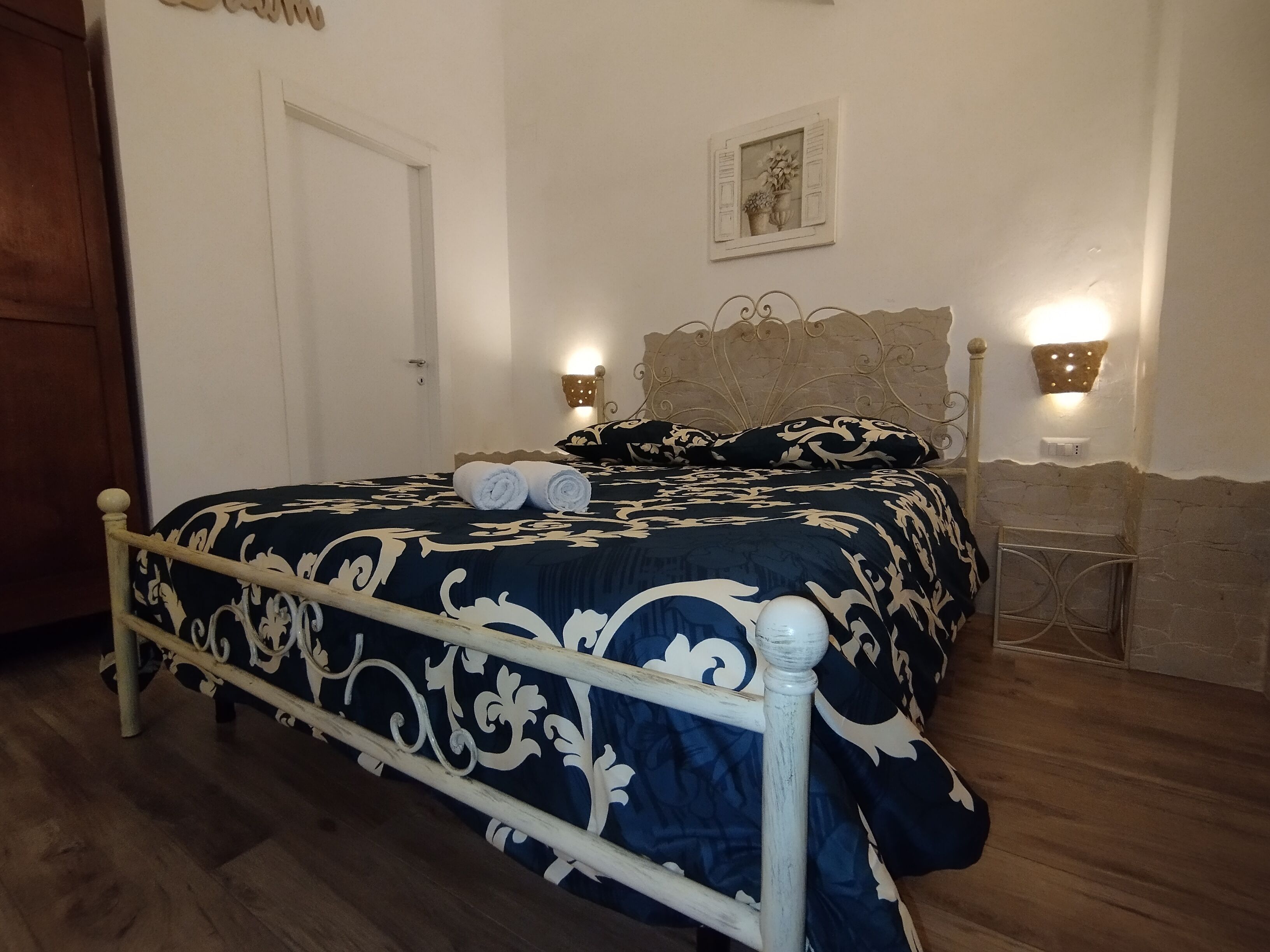 A bedroom with a bed, a wooden door, a wall-mounted light fixture, and a small table.