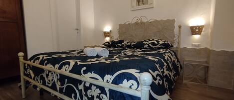 A bedroom with a bed, a wooden door, a wall-mounted light fixture, and a small table.