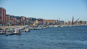 A marina with boats docked, buildings in the background, and a clear sky. - Ap1 Valdés de Avilés (Avilés)