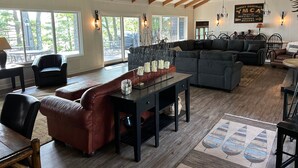 Een ruime woonkamer met een hoge plafond, grote ramen en een combinatie van zitplaatsen, waaronder banken en fauteuils.