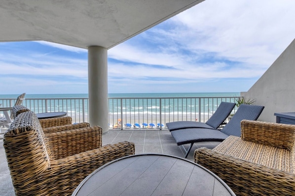 A balcony with wicker furniture, a table, and a view of the ocean.