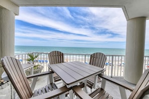 A balcony with a view of the beach and ocean, featuring a table and chairs.