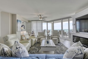 A spacious living room with a large window, a ceiling fan, and a fireplace.