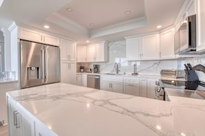 A modern kitchen with white cabinetry, a marble countertop, stainless steel appliances, and a built-in oven.