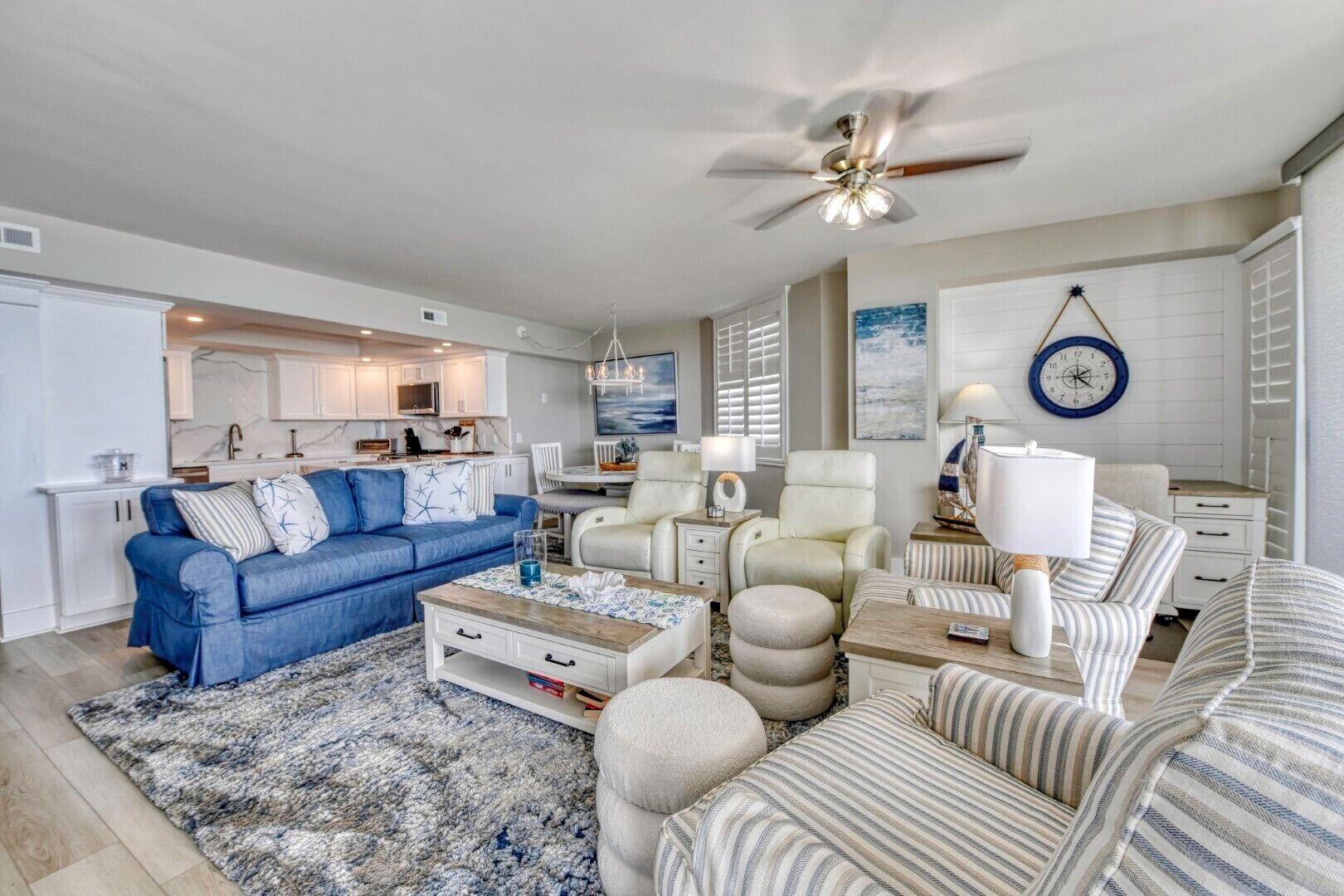 A modern living room with a blue sofa, a white armchair, a striped sofa, a coffee table, and a ceiling fan.