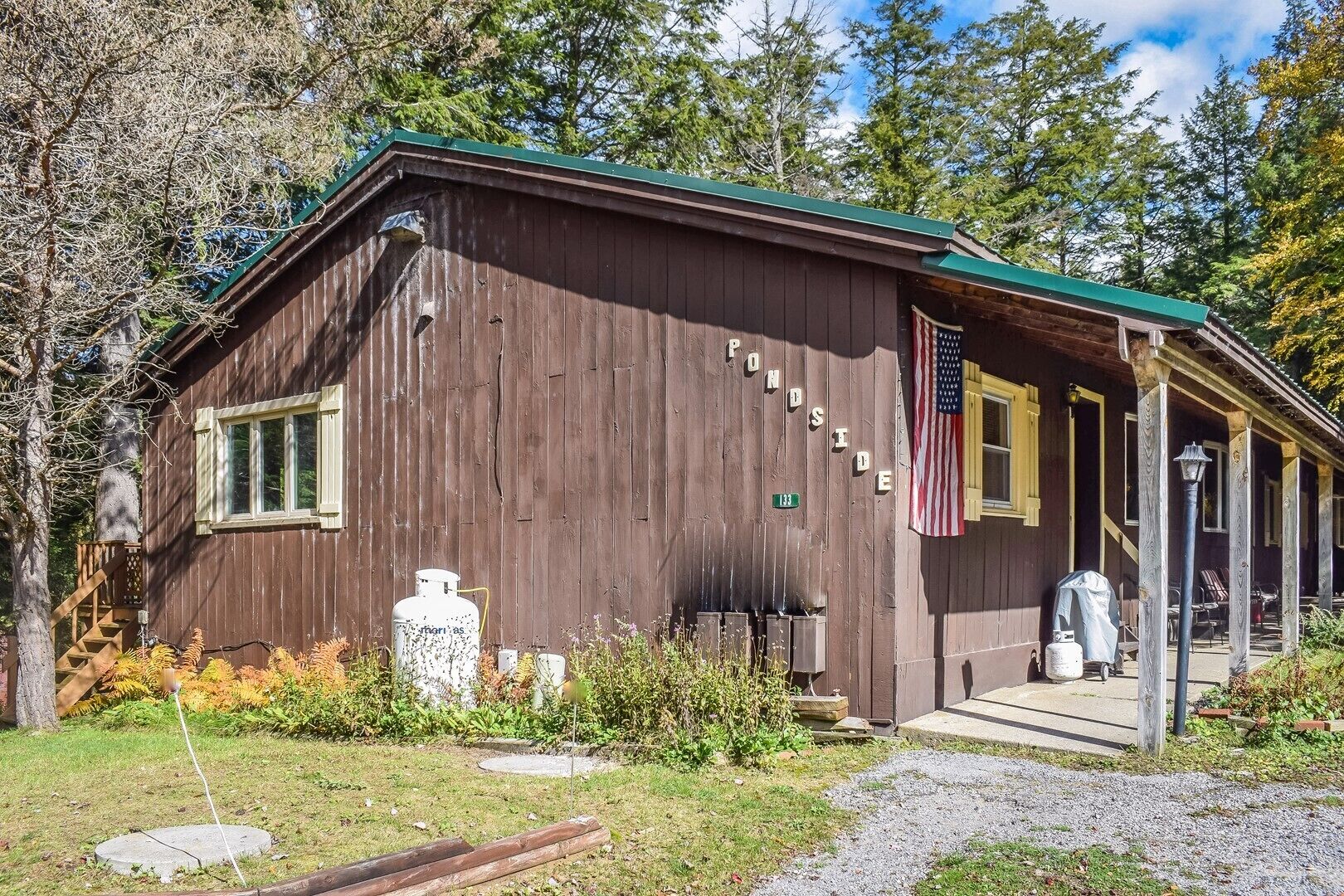 A rustic wooden cabin with a porch, a flag, and a mailbox.