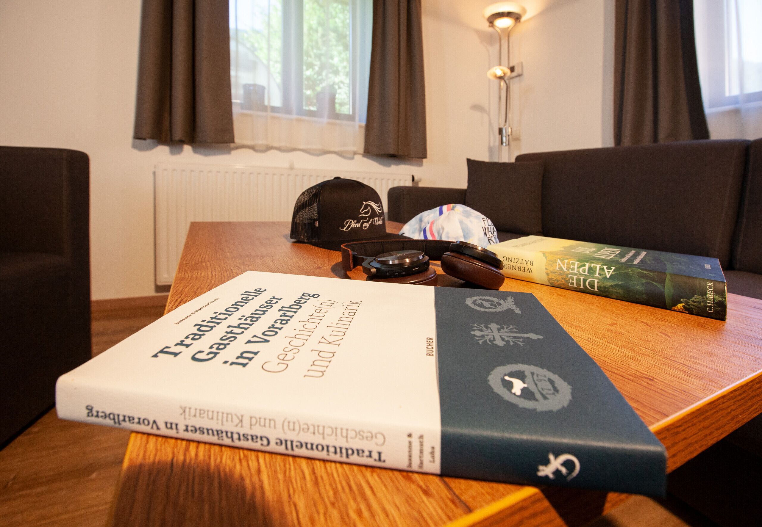 A wooden table with books, a cap, and a remote control.