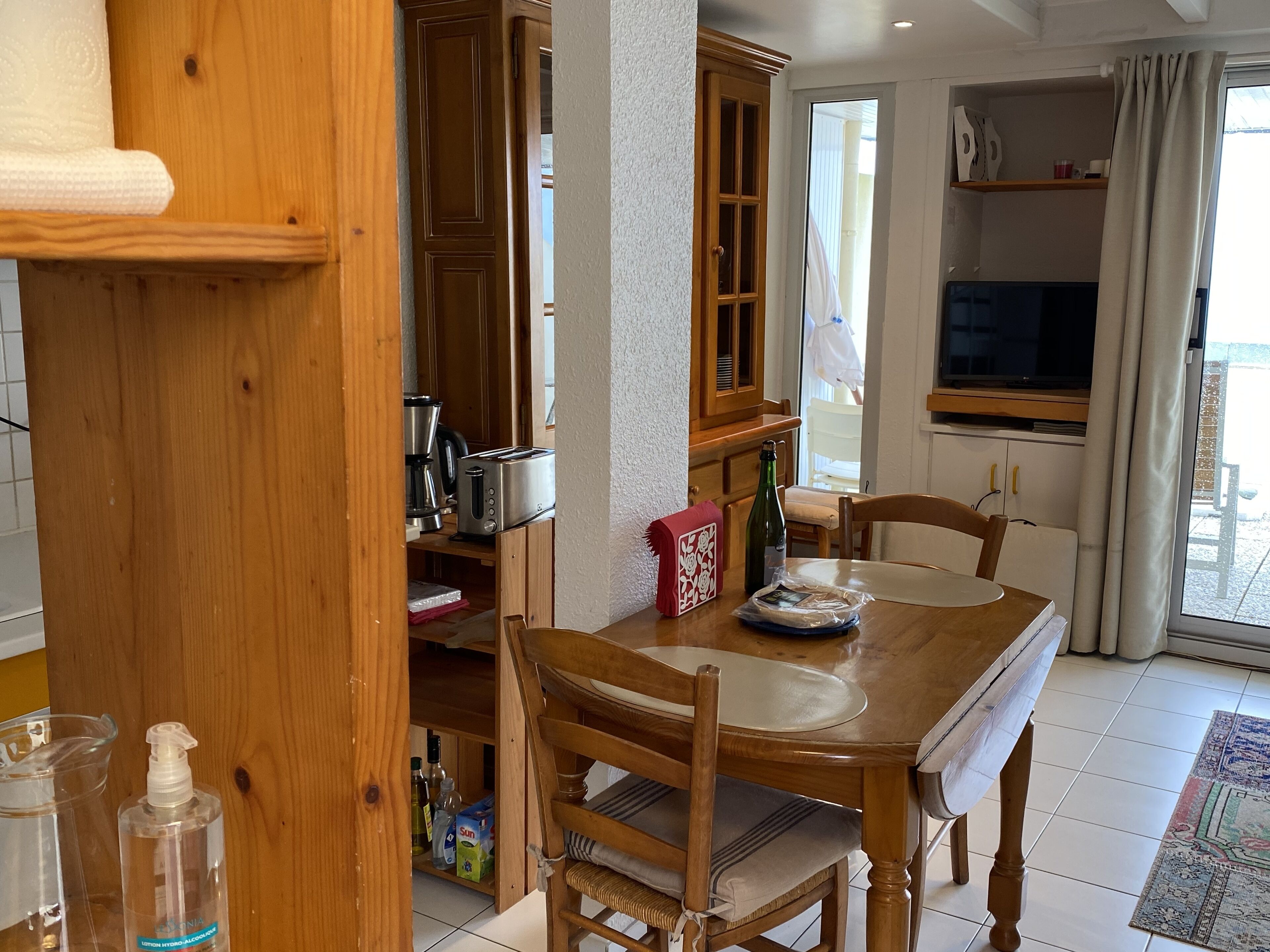 Un tavolo da pranzo in legno con sedie, angolo cottura con mobili e elettrodomestici, e una finestra con tende.