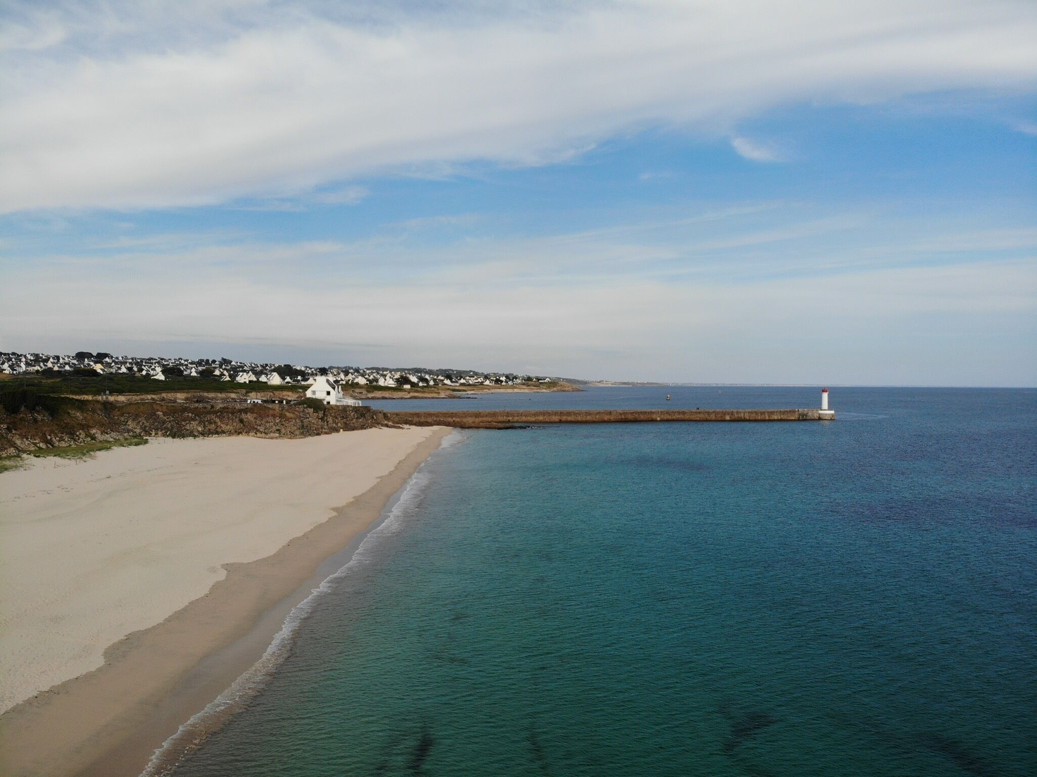 A coastal beach with a lighthouse, sandy shore, and white buildings in the background.