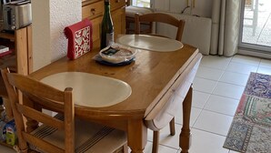 Un comedor con una mesa y sillas de madera, un armario con puertas de vidrio, un televisor sobre un mueble bajo y vistas a través de una ventana con cortinas.