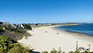 Una playa extensa con gente tomando el sol y nadando, rodeada de casas y vegetación.