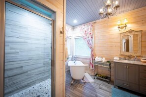 Un baño con una bañera de patas de león, paredes de madera, un espejo grande y una zona de ducha.