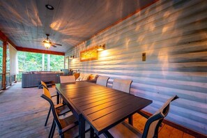 Una terraza de madera con una mesa, sillas, un ventilador de techo y vistas al exterior.