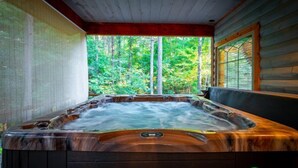 Een hottub met een houten buitenkant, omgeven door een houten terras en uitzicht op een bos.