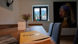 Ein Holztisch mit einer Zeitschrift, einer Vase mit Blumen und einem Fenster mit Blick auf Gebäude.