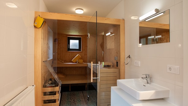 Ein modernes Badezimmer mit Holzvertäfelung, einer Duschkabine aus Glas und einem weißen Waschbecken.