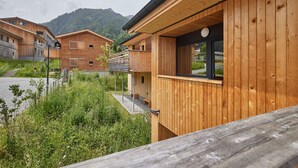 A wooden cabin-style building with a balcony, surrounded by greenery and mountains in the background. - 46282 Montan 28 OG (St. Gallenkirch)