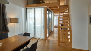 A wooden interior with a dining table, chairs, a lamp, a staircase, and a view through large glass doors. - 46282 Montan 28 OG (St. Gallenkirch)