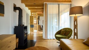 A cozy living room with a wooden floor, a sofa, a green armchair, a lamp, and a fireplace. - 46282 Montan 28 OG (St. Gallenkirch)