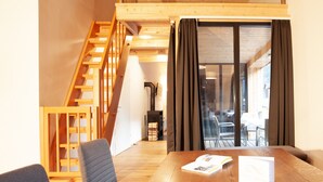 A modern interior with a wooden staircase, a dining area with a table and chairs, and a view through a glass door.
