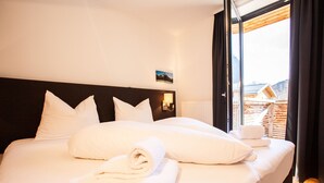 A hotel room with a large bed, white linens, and a view of a mountain through the window.