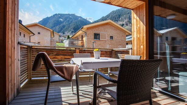 A wooden deck with a table and chairs, overlooking a mountain landscape.