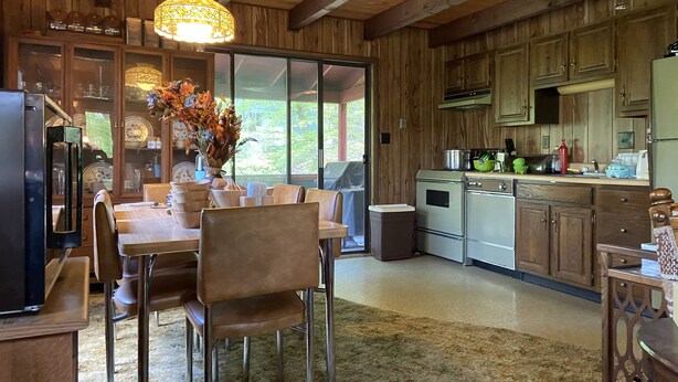 A rustic kitchen with wooden cabinets, a dining area with a table and chairs, and a large window providing a view of greenery outside. - 4br 2ba Chalet in Poconos that sleeps 10 (Bushkill)