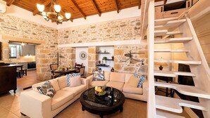 Un salon chaleureux avec un mur en pierre, un plafond en bois et un escalier.