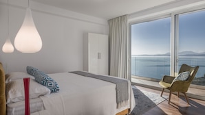 Quarto com cama, uma cadeira, guarda-roupa e uma janela grande com vista para o mar.