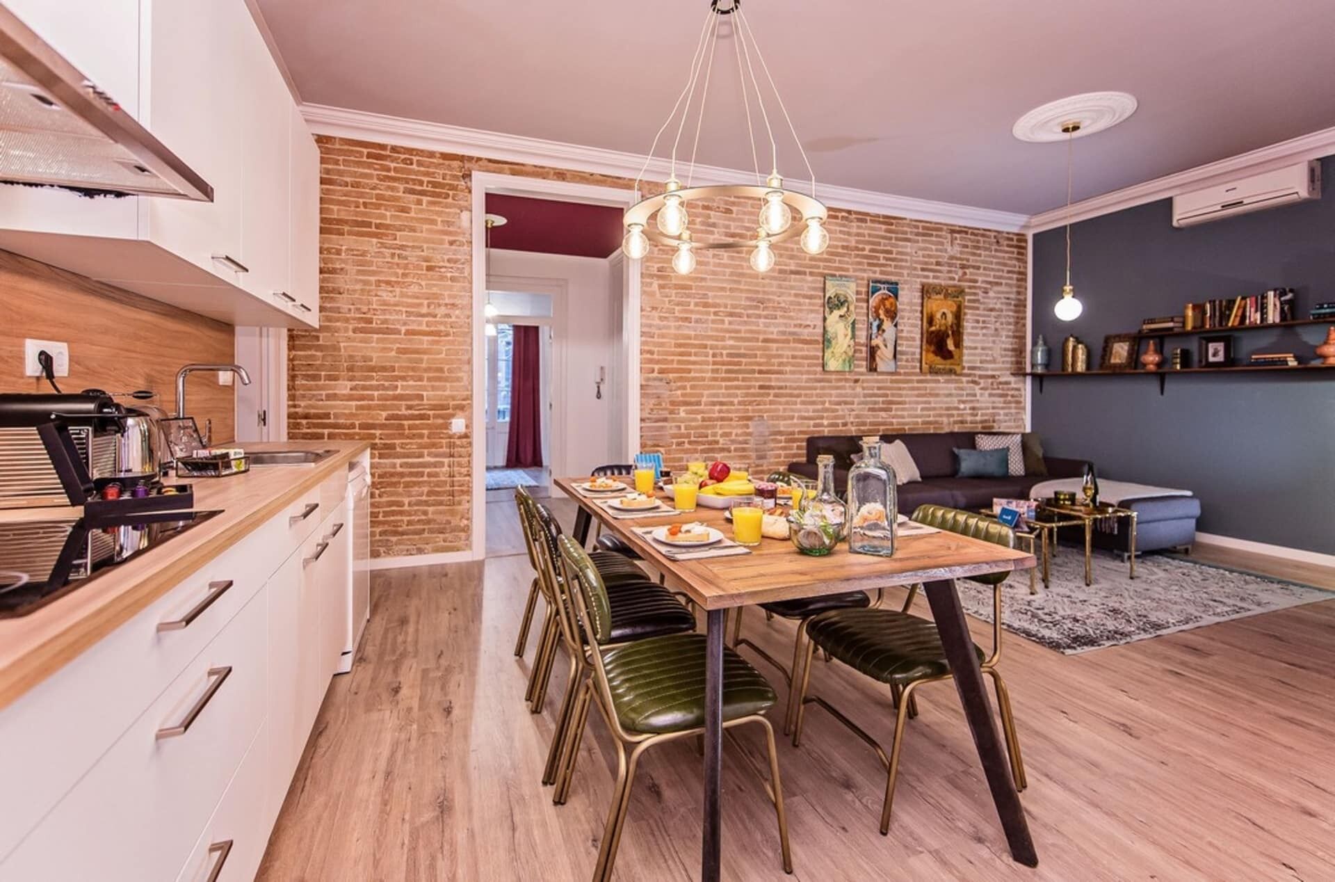 Una cocina moderna con comedor, que presenta una pared de ladrillo, una araña y una mesa de comedor preparada para seis personas.
