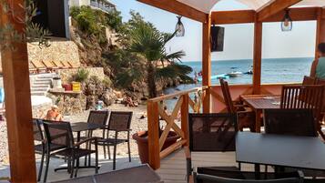 A wooden deck with outdoor seating overlooking a rocky beach and the sea.