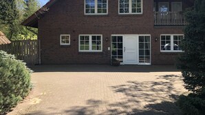 A two-story brick house with a large front porch, a wooden fence, and a paved driveway.