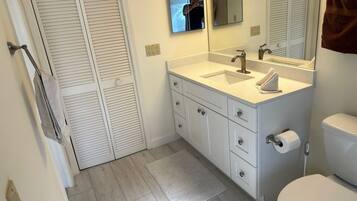 A bathroom with a white sink, mirror, and toilet. There is a towel hanging on the wall and a mat on the floor.