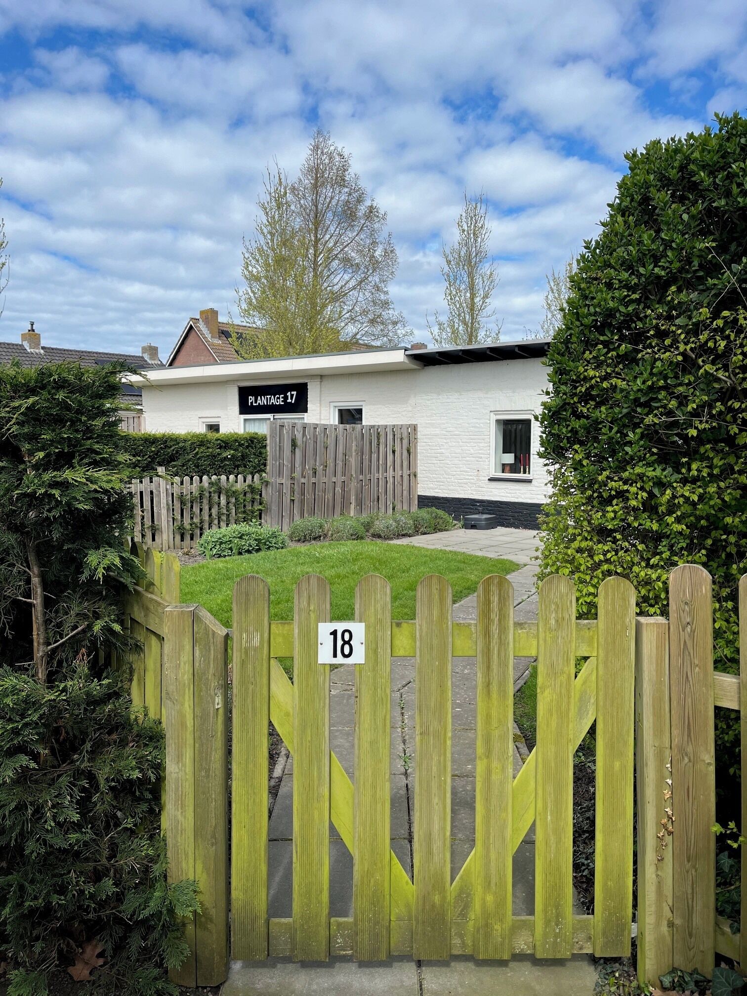 A residential building with a sign reading 'PLANTAGE 17' and a wooden gate with the number '18'.
