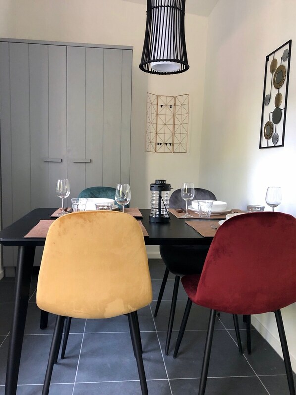 Un coin repas avec une table dressée pour quatre personnes, comprenant deux chaises aux revêtements contrastés, un luminaire suspendu moderne et un élément décoratif mural.