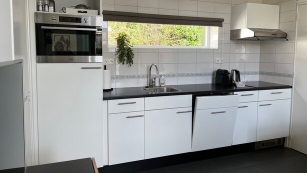 A modern kitchen with white cabinets, a black countertop, a built-in oven, a window, and a black stove. - Compact, trendy furnished, vacation bungalow. Enclosed garden. Pets welcome! (Bruinisse)