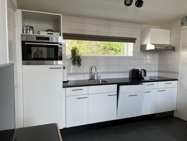 A modern kitchen with white cabinets, a black countertop, a built-in oven, a window, and a black stove. - Compact, trendy furnished, vacation bungalow. Enclosed garden. Pets welcome! (Bruinisse)