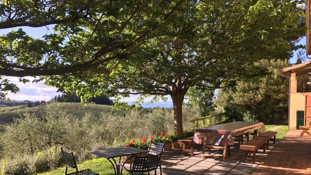Un pati exterior amb taula i cadires, envoltat de vegetació exuberant i vistes al camp.