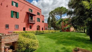 Edifici vermell amb persianes verdes, estructura de maó amb una finestra, i un jardí ben cuidat.