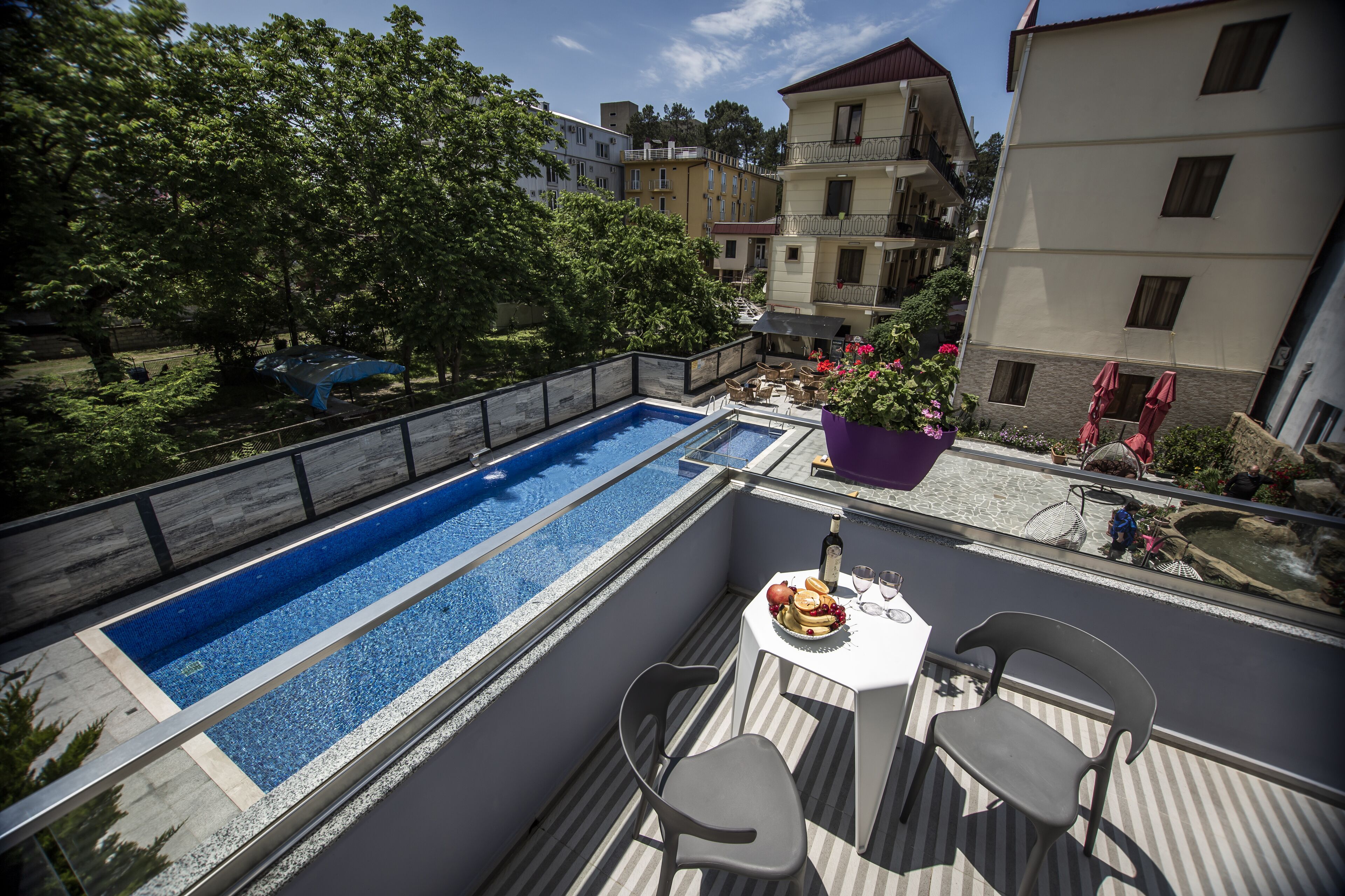 Una piscina en la azotea con una mesa y sillas, rodeada de edificios y árboles.