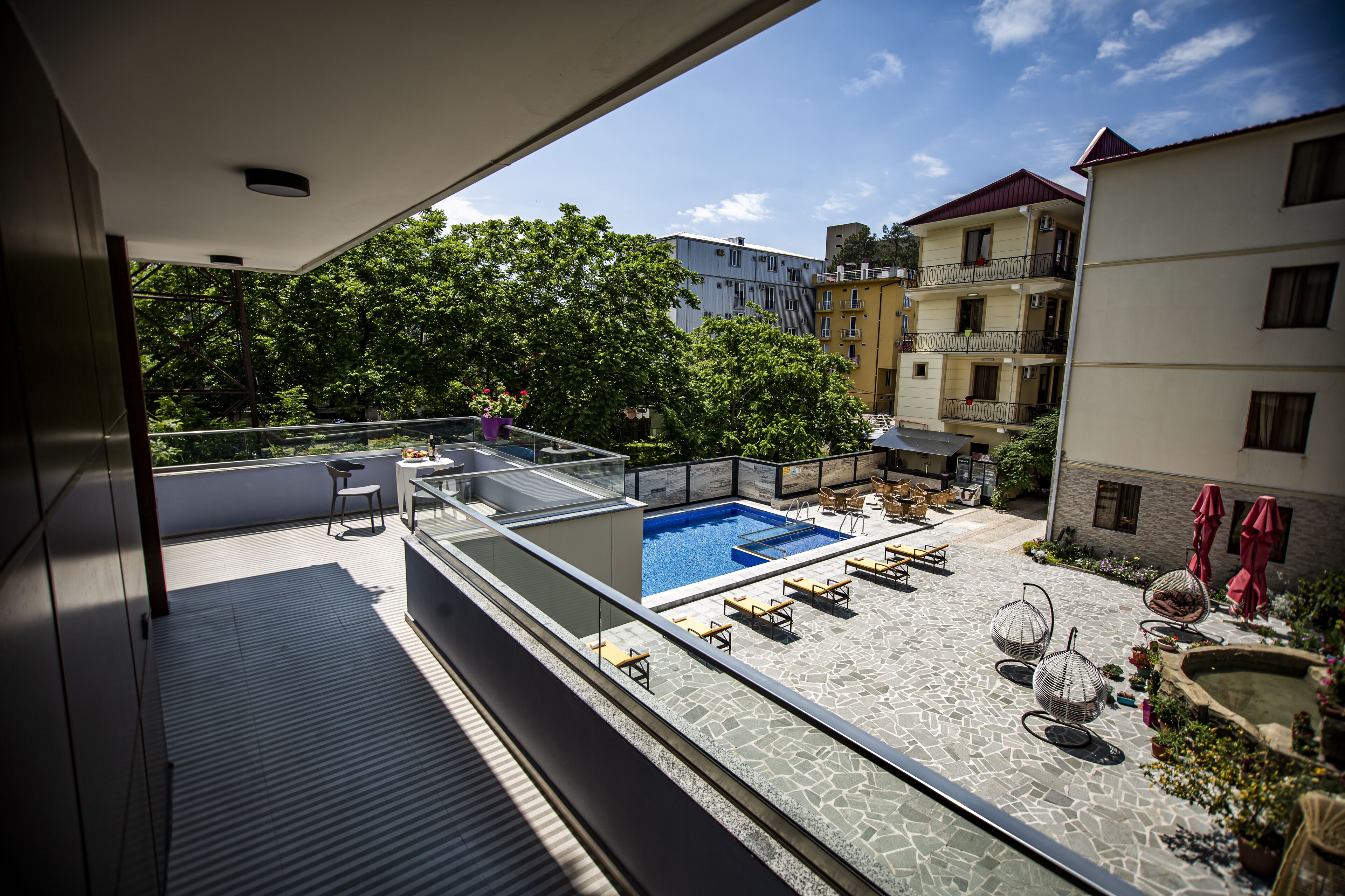 A rooftop pool area with lounge chairs and a small pool, surrounded by buildings and trees.