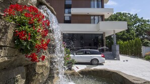 Een modern gebouw met een meerlaags balkon, een waterval en een vijver met bloemen.