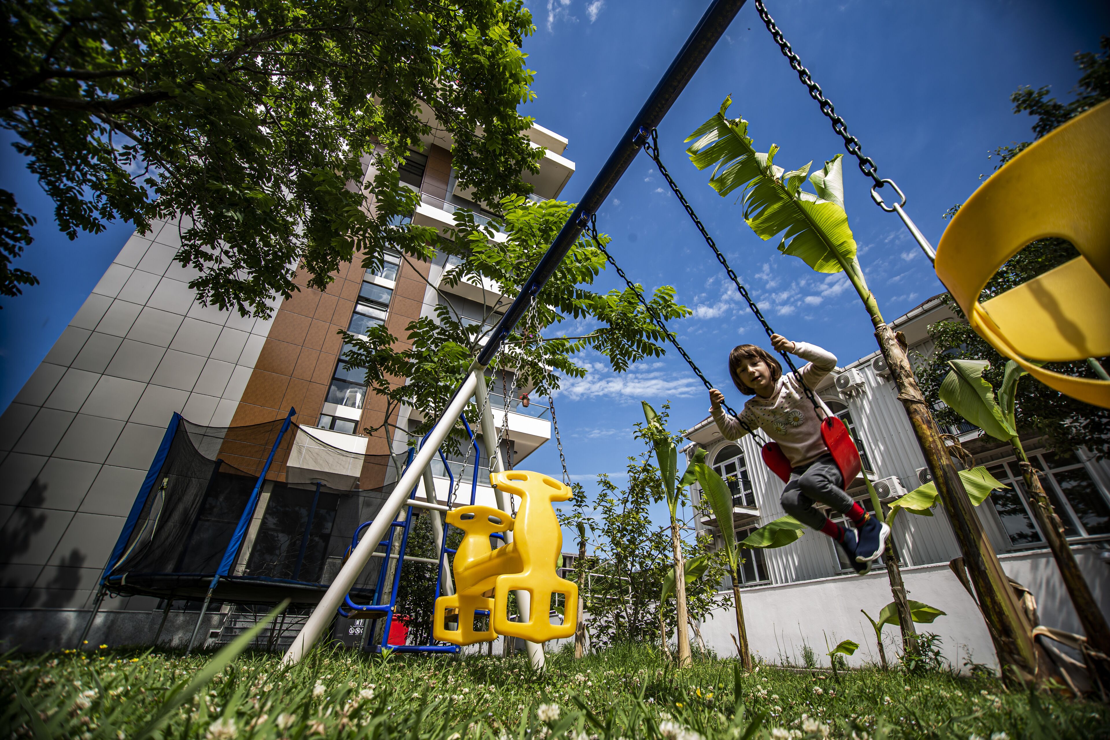 A child on a swing set in an outdoor area with a building in the background.