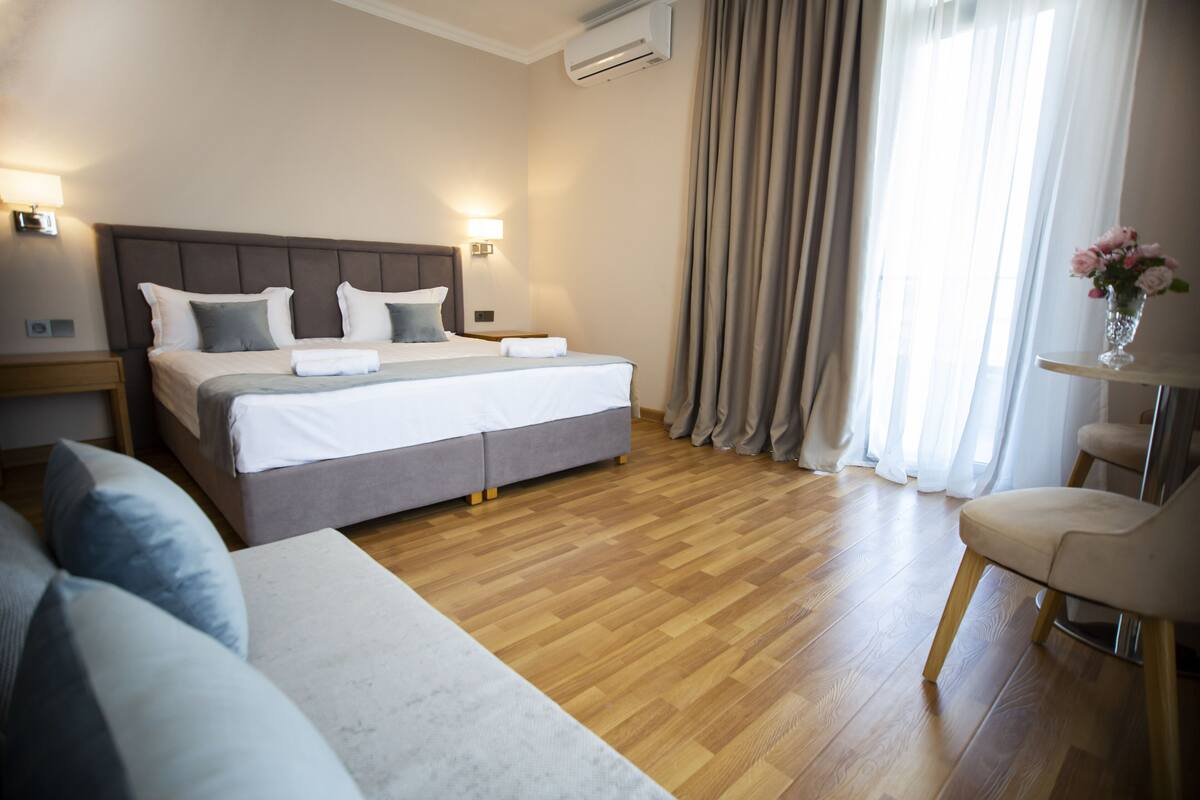 Une chambre d’hôtel avec un grand lit, une table de chevet, une chaise et une fenêtre avec des rideaux.