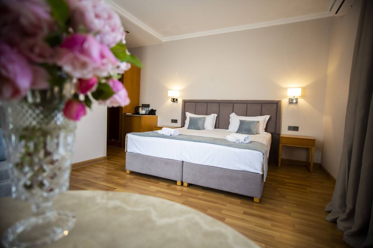 Une chambre d’hôtel avec un lit, des tables de chevet, un vase avec des fleurs et un plancher en bois.