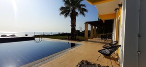 Ein Pool mit Meerblick, eine Palme und Sitzmöglichkeiten im Freien.
