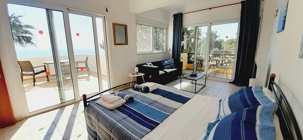 A room with a bed, a sofa, a small table, and a balcony with a view.
